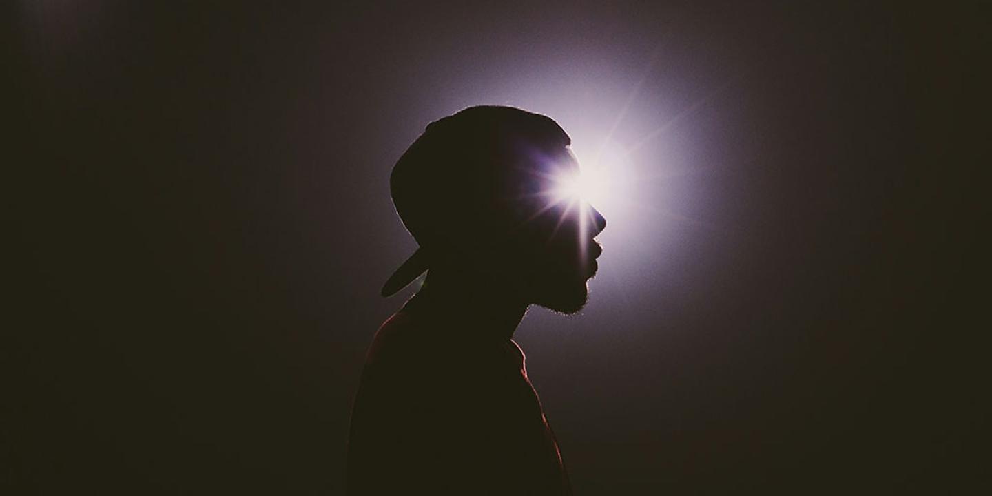 A star burst of light appears to emanate from the eye of a man's head in silhouette.