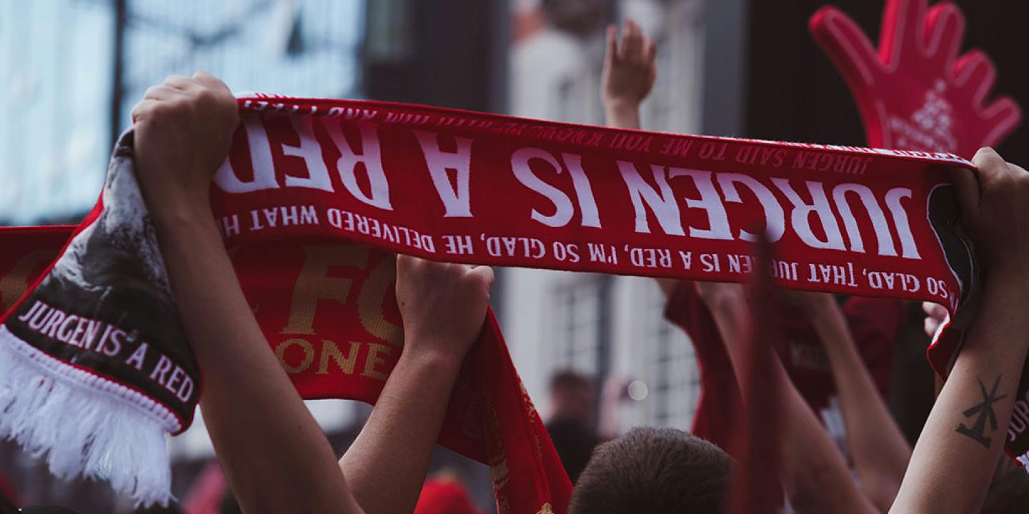 A fan holds an upside down football scrarf that reads 'Juergen is a red'.