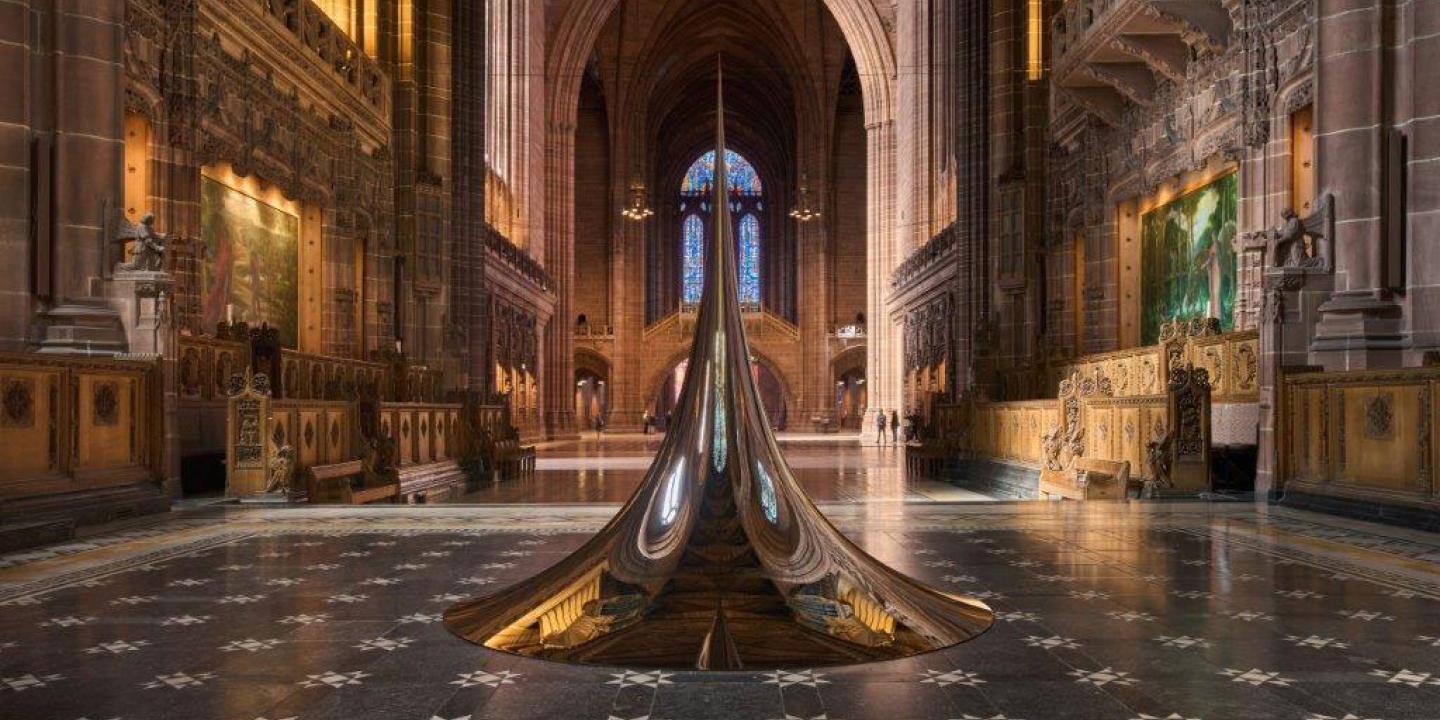 An art structure of a circular peak sits on the chequered floor of a cathedral.