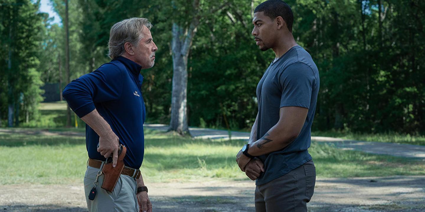 Two men stand off against each other, one holds a holstered gun.