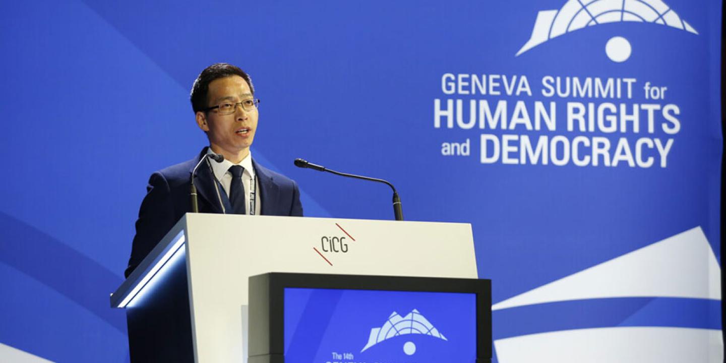 A conference speaker at a podium against a backdrop of blue.