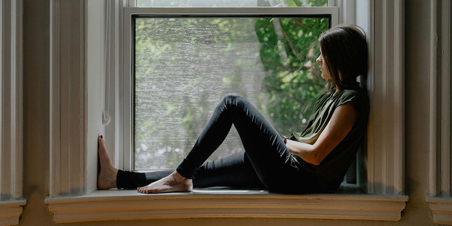 A person sits on a window sill with one raise knee.