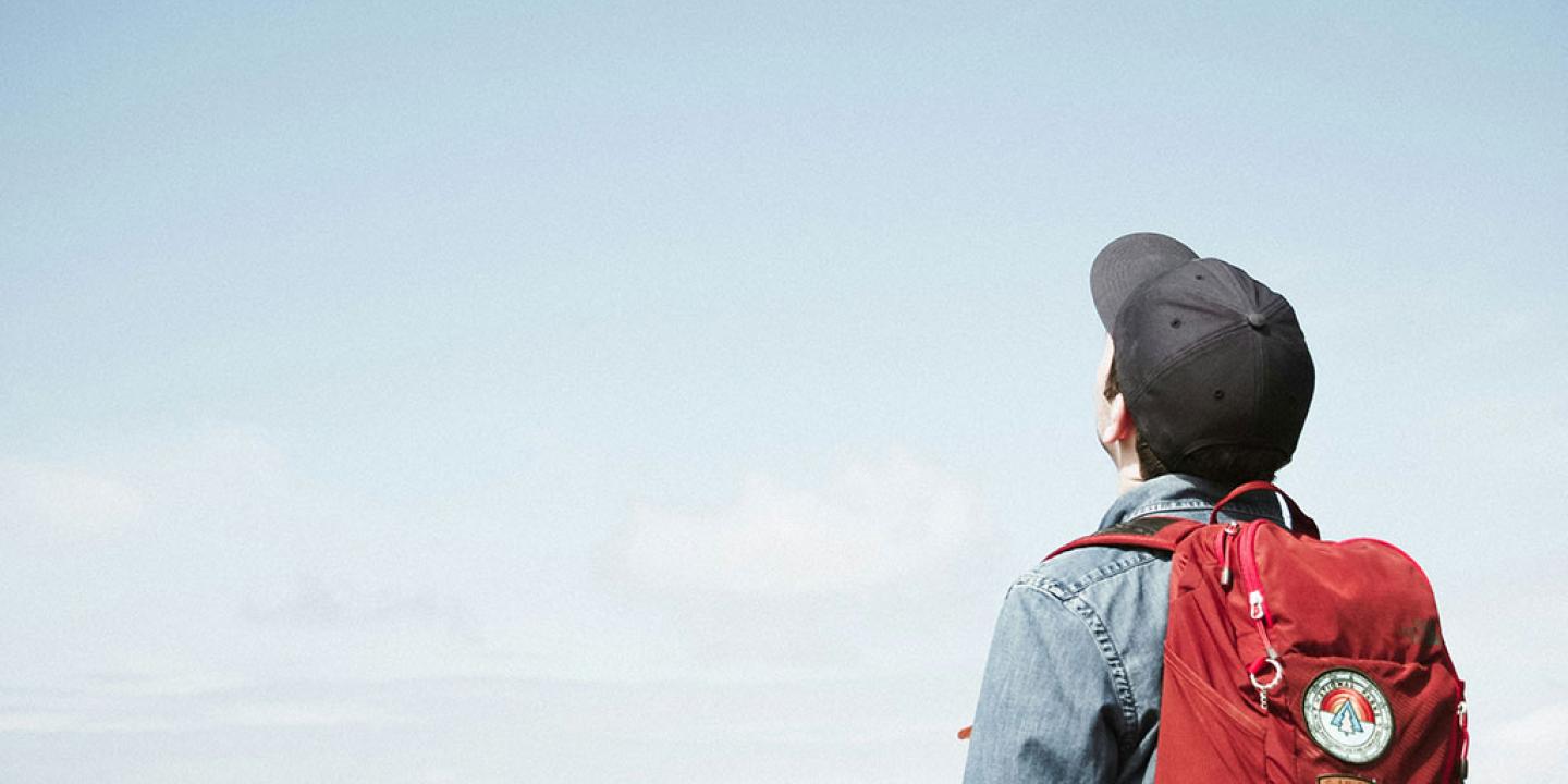 A person wearing a backpack looks to the sky.