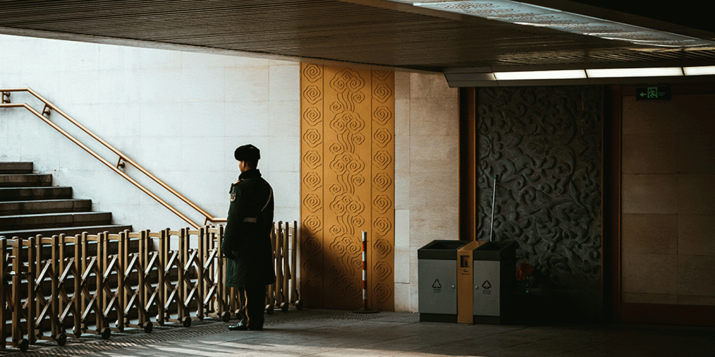 A guard stands behind a barrier across an entrance to a station escalator.