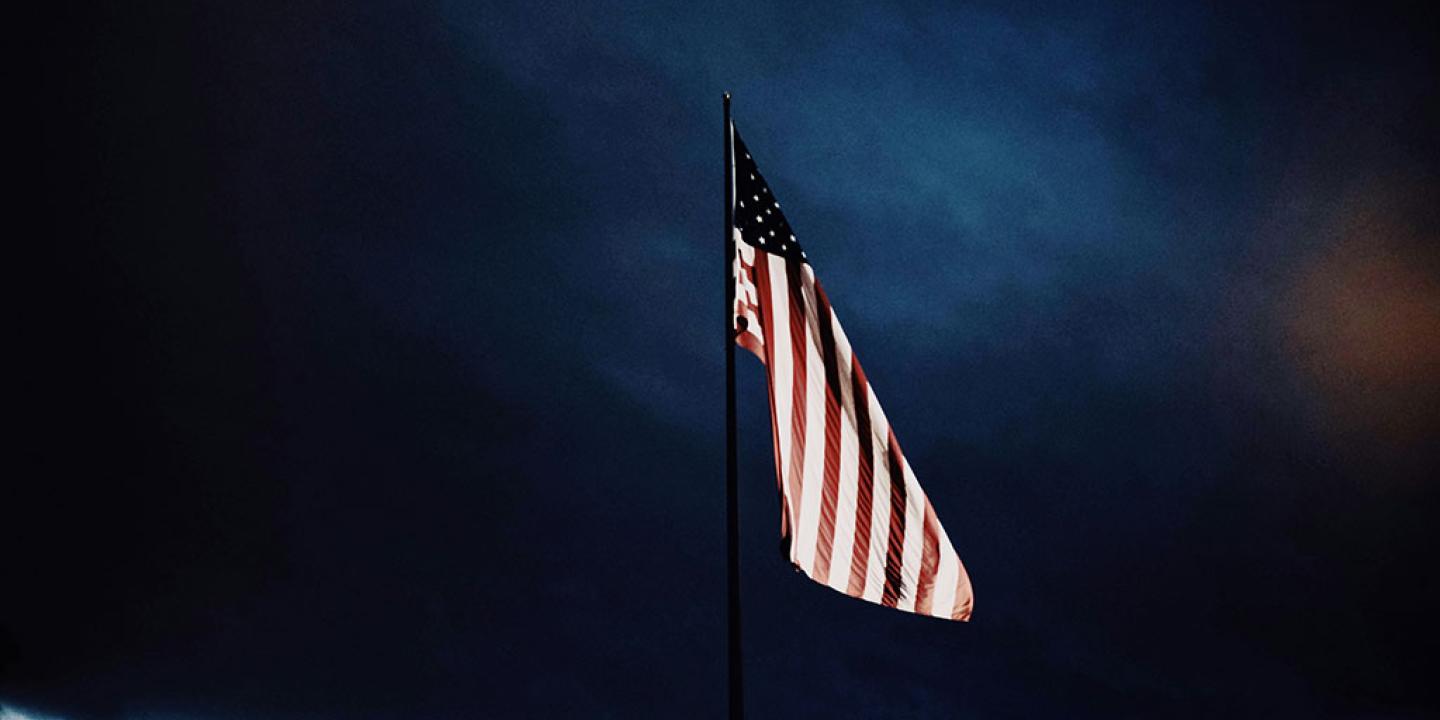 A US flag flutters under a dark brooding cloudy sky.