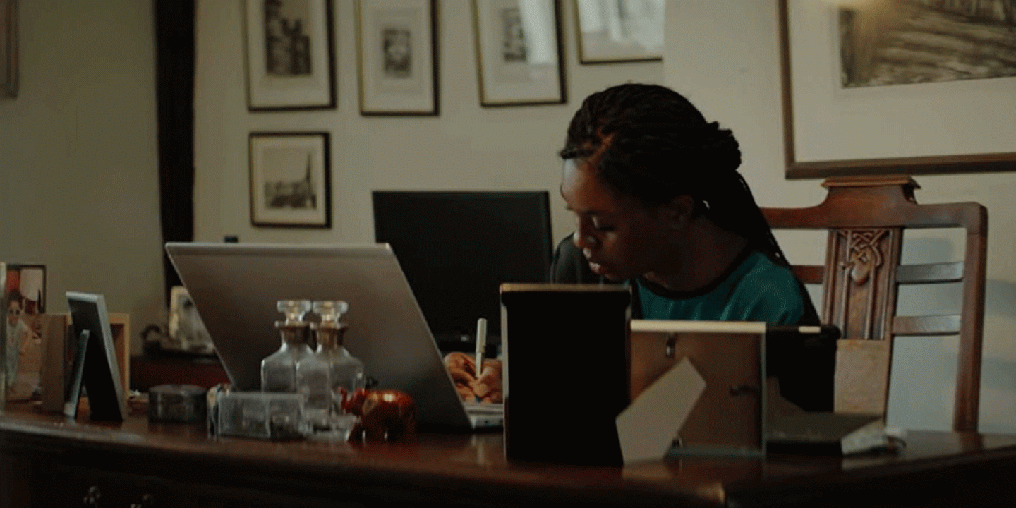 A woman works at a laptop on a desk surrounded by picture frame.