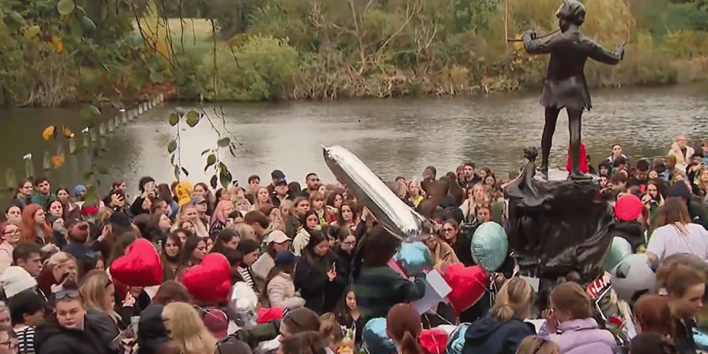 A crowd of teenagers gather by a Peter Pan statue to mourn a dead pop star