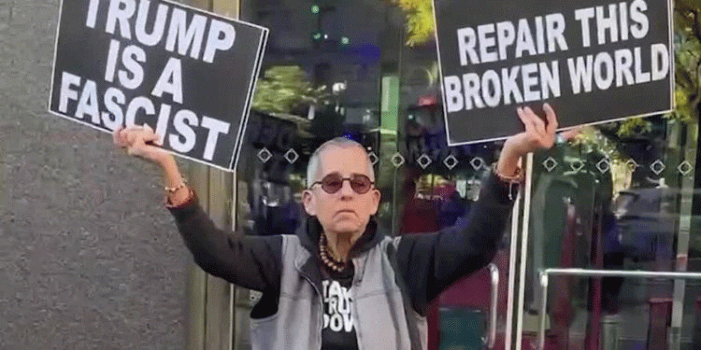 A protester holds placards up in both hands. One reads: Trump is a fascist. The other: Repair the broken world 