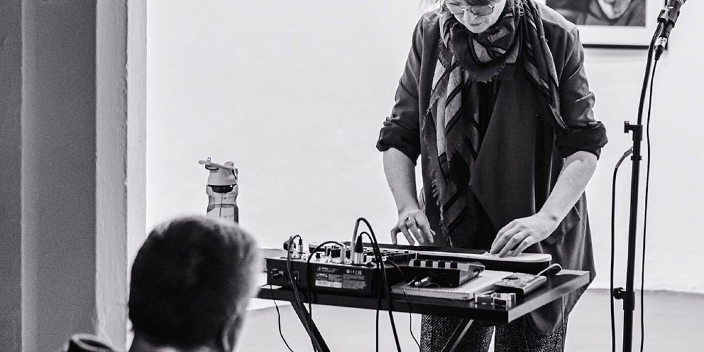 A woman stand at a mixing desk playing a small keyboard.