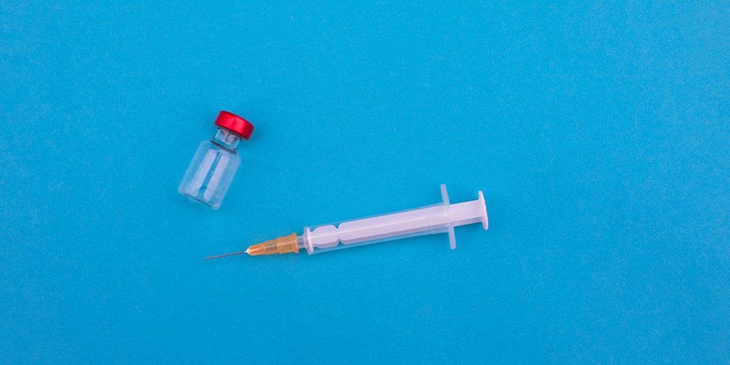 A vial and syringe lie on a blue backdrop.