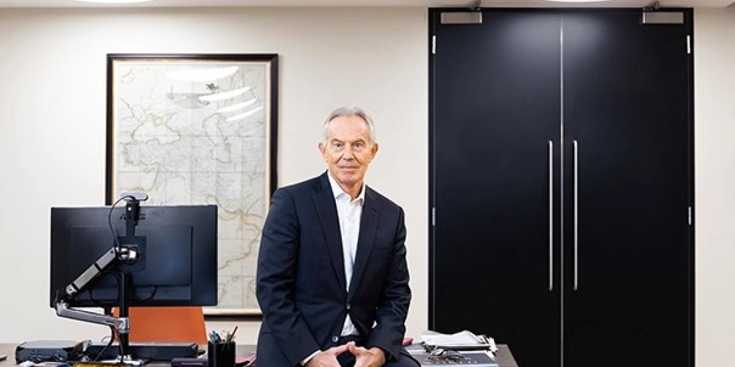 Tony Blair rests on the edge of a desk.