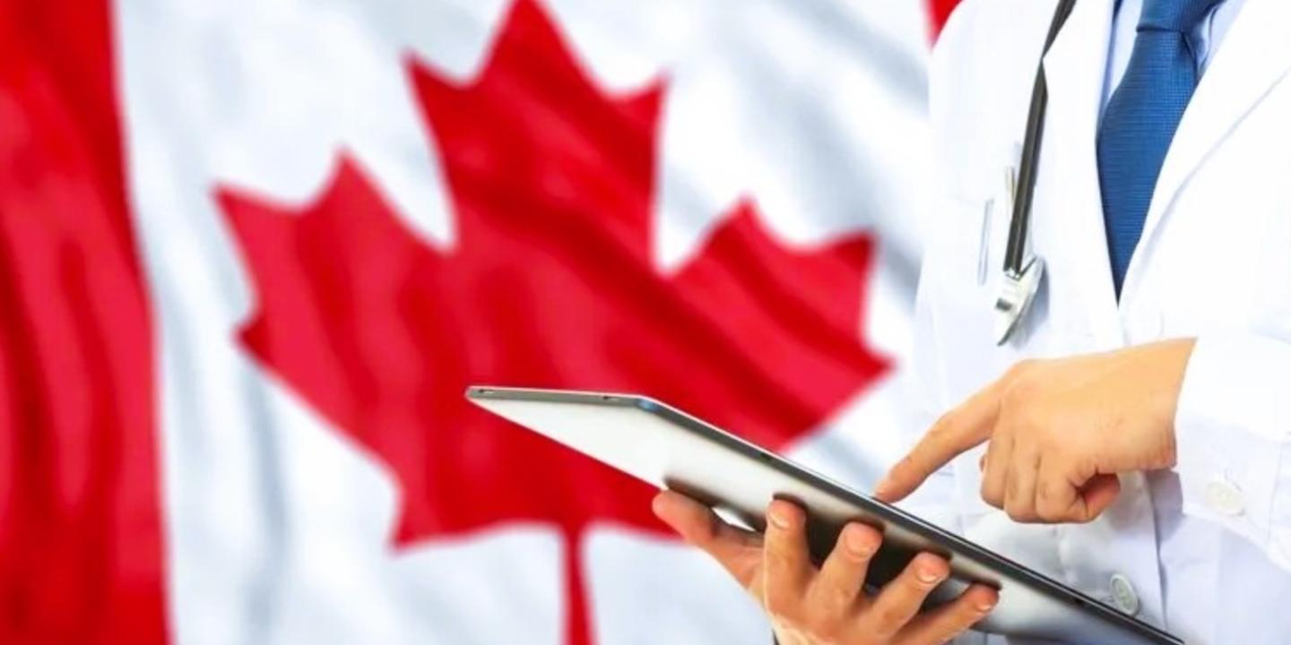 a doctor consults a tablet against the backdrop of a Canadian flag.