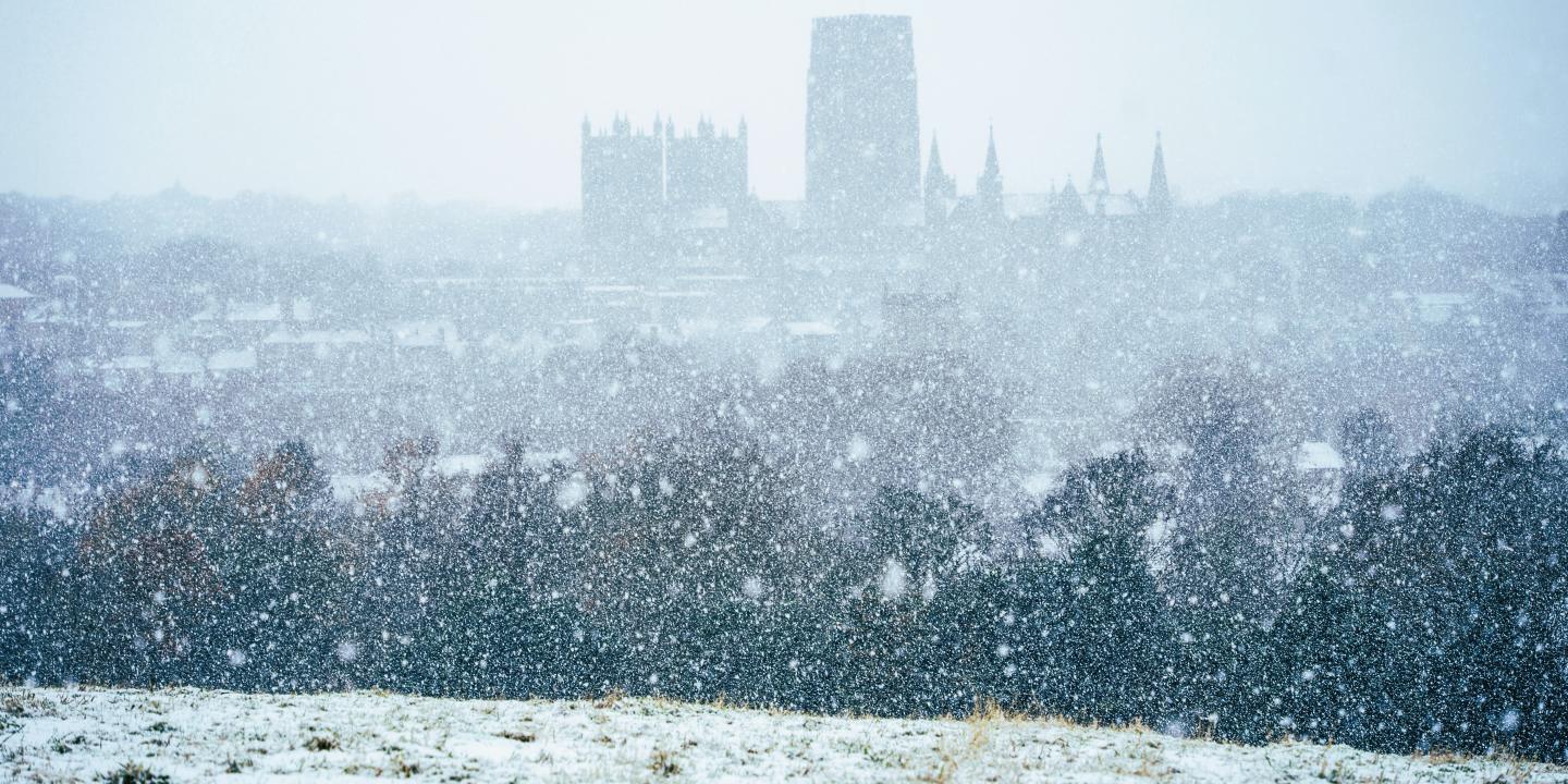 Snow falling pixilates the view from a hill towards Durham Cathedral.