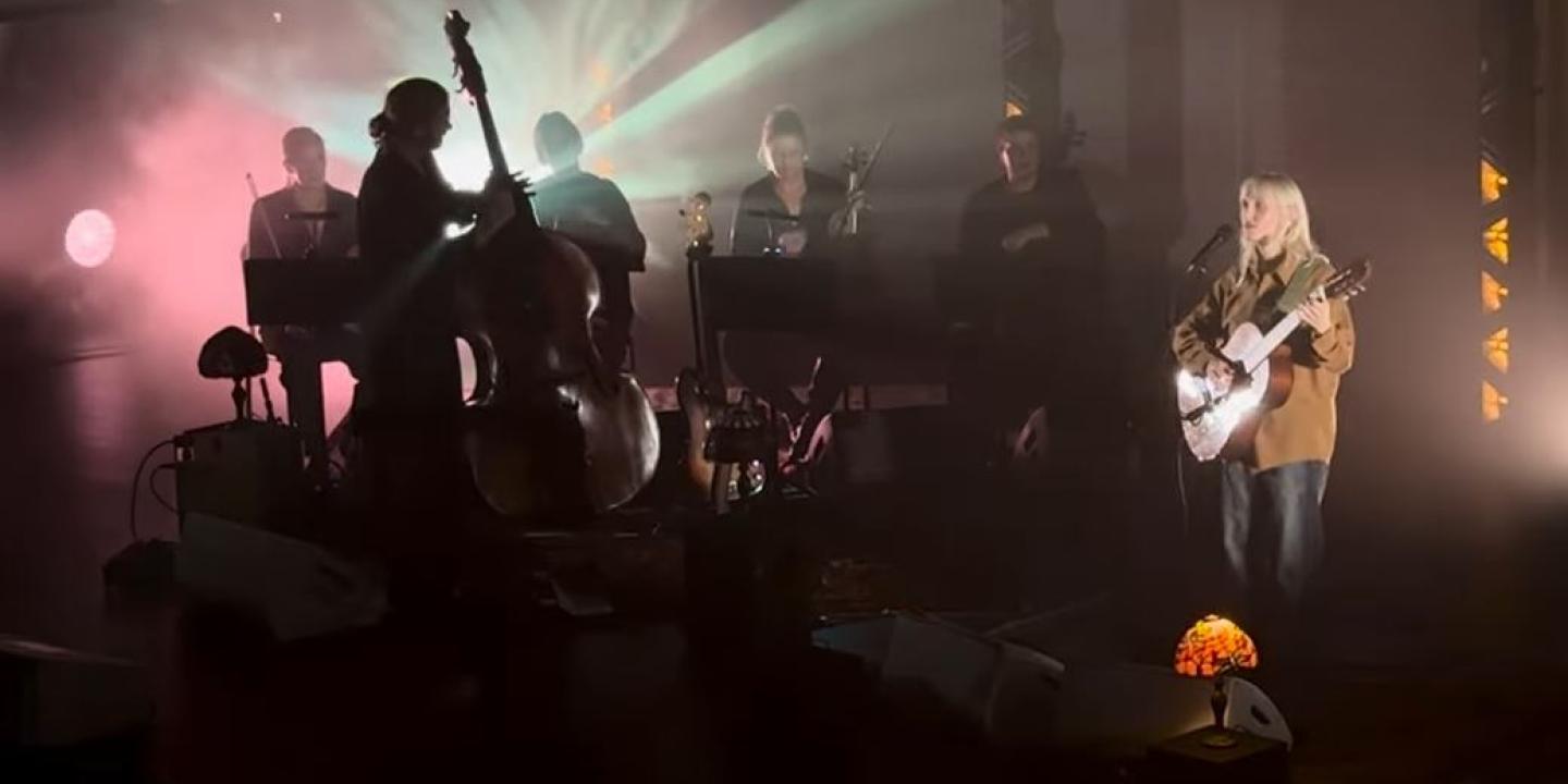 A misty back lit stage hosts a singing guitarist and a double base player