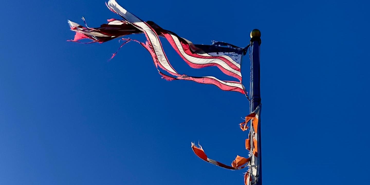 a tattered American flag flies against a blue sky.