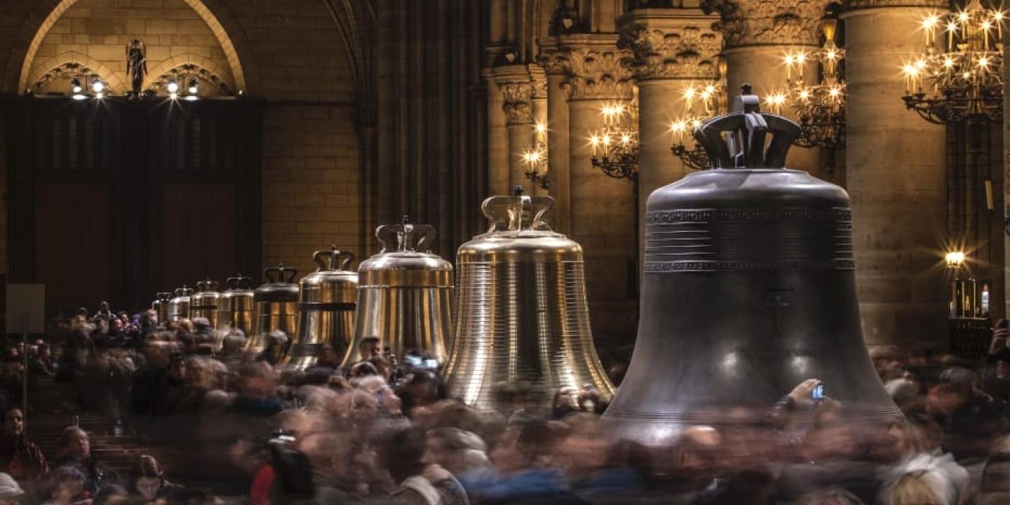 Restored church bells lined up in a cathedral, as crowds mill around them.