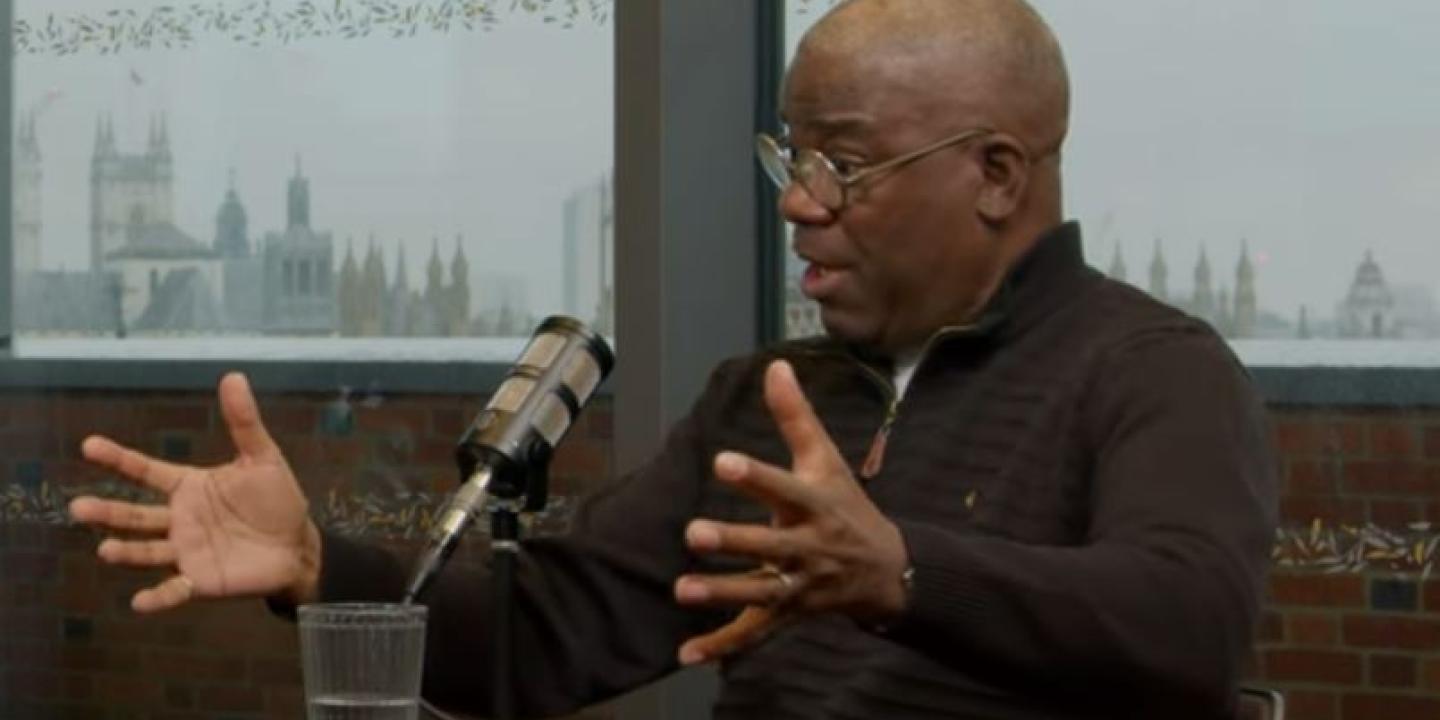 A podcast guest talks in front of a mic, while gesturing with both hands.