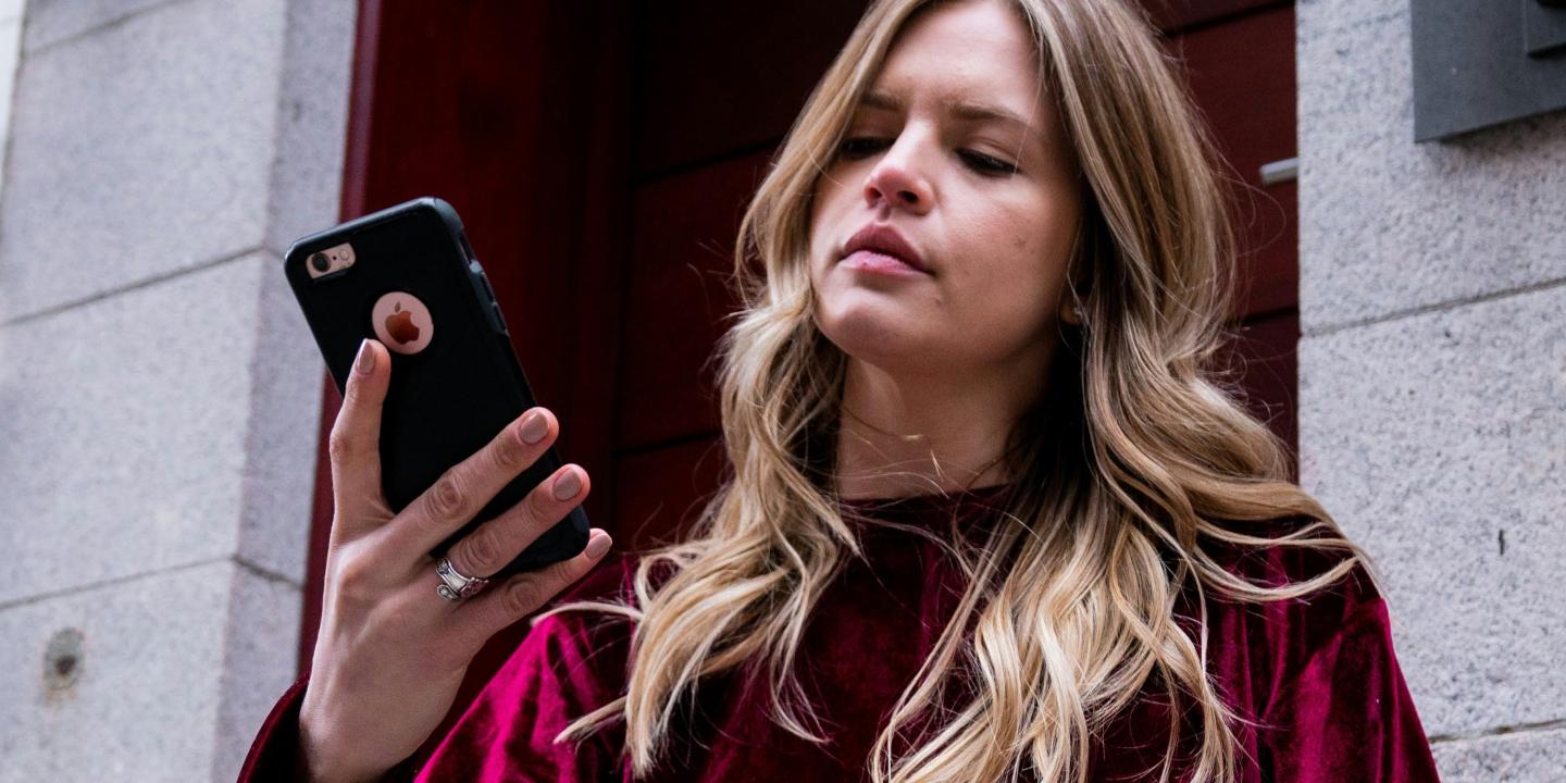 A woman holds her phone up in her hands and looks at it in a slightly vexed way.