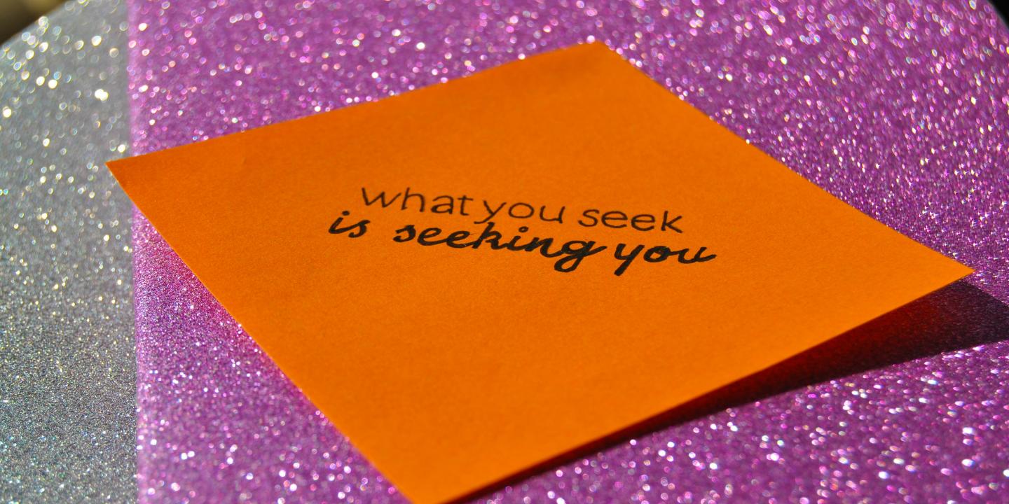 Against a purple glittery background, a orange notelet reads: 'what you seek is seeking you.'