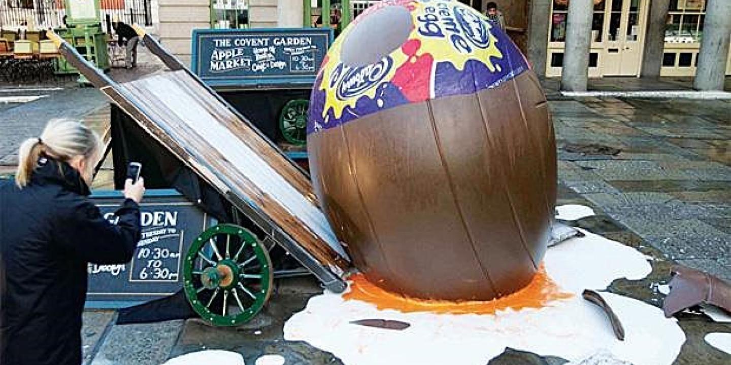 A giant creme egg lies smashed on the ground beside a tilted market barrow.