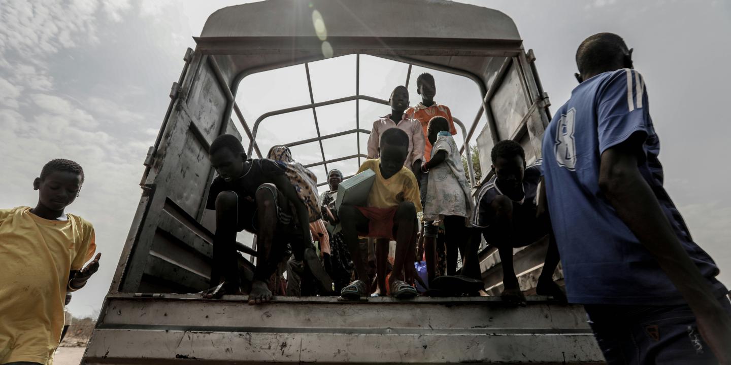 Refugees stand at the back of an open truck.