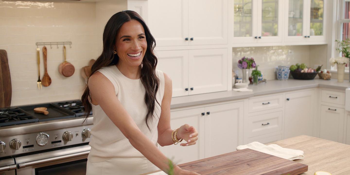 A woman stands at a kitchen island with a chopping board on it.