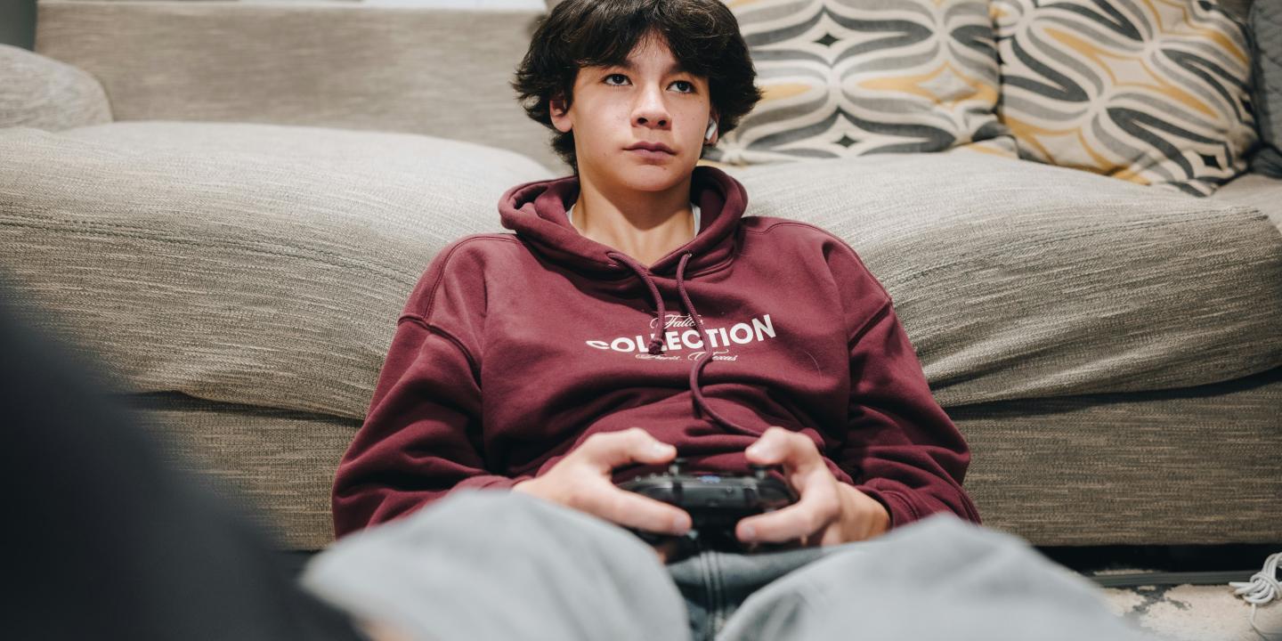 A teenager slumped against a sofa plays a video game