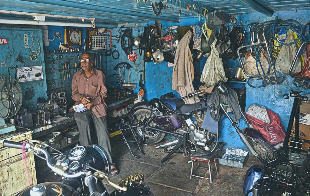 A mechanic stands in a workshop beside a motorcycle under repair.