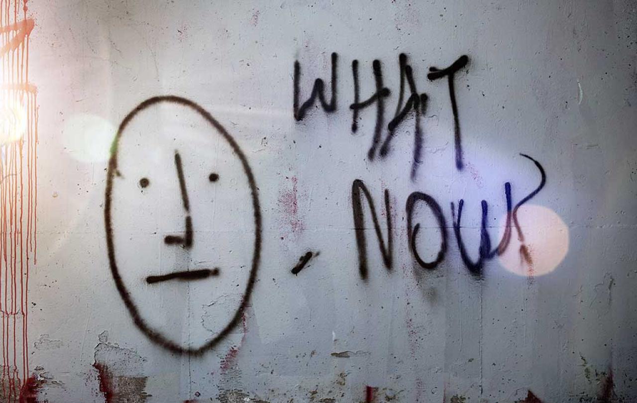 A graffited wall shows a stick man face next to 'what now'