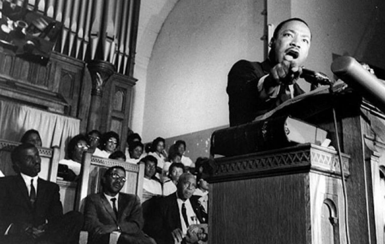 Martin Luther King reaches from the pulpit of a church while he preaches.