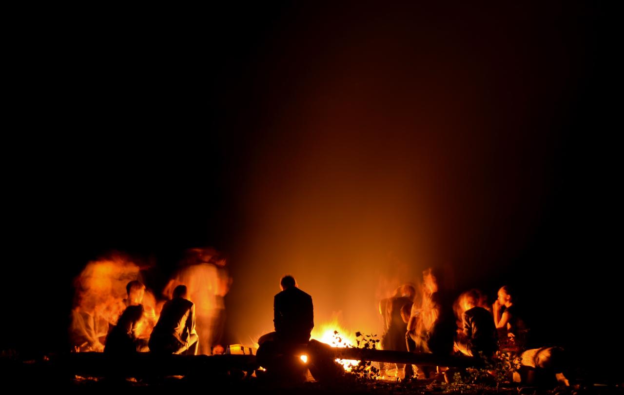 People sitting around a campfire are silhouetted against the night.