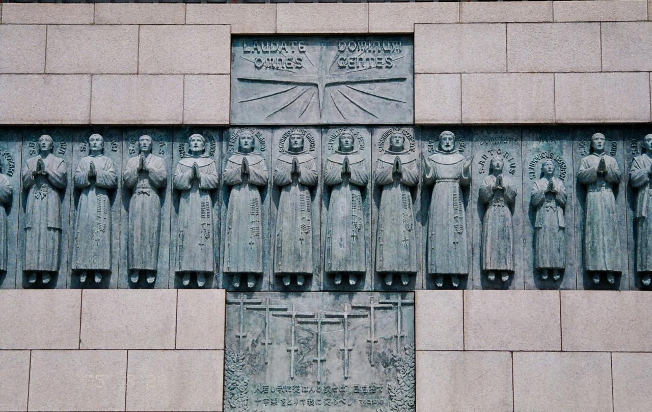 A stone monument within which set, in the shape of a cross are statues of numerous standing praying figures.