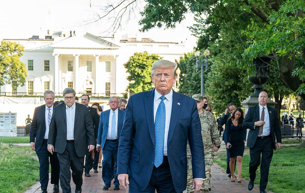 A fierce looking man walks at the head of a phalanx of suited men.