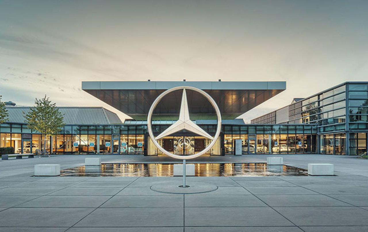 A large sculpture of the Mercedes Benz three-point star stands in front of a large, low glass fronted showroom.