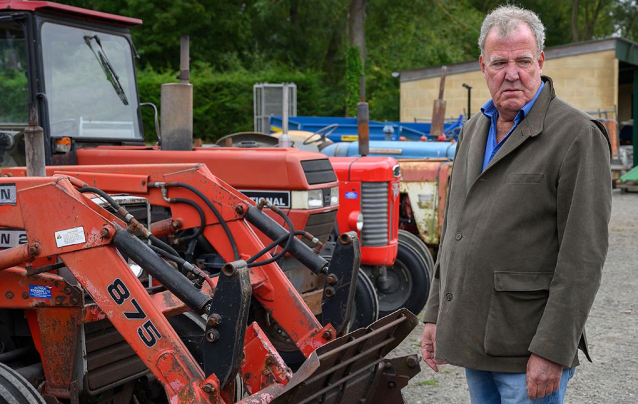 A man stands looking baleful next to a row of red tractors