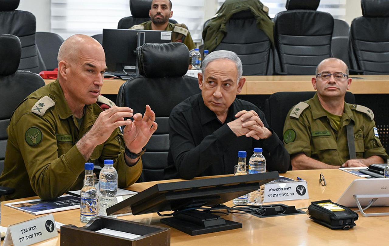 Between two generals wearing camouflage uniforms, a man in a black shirt listens.