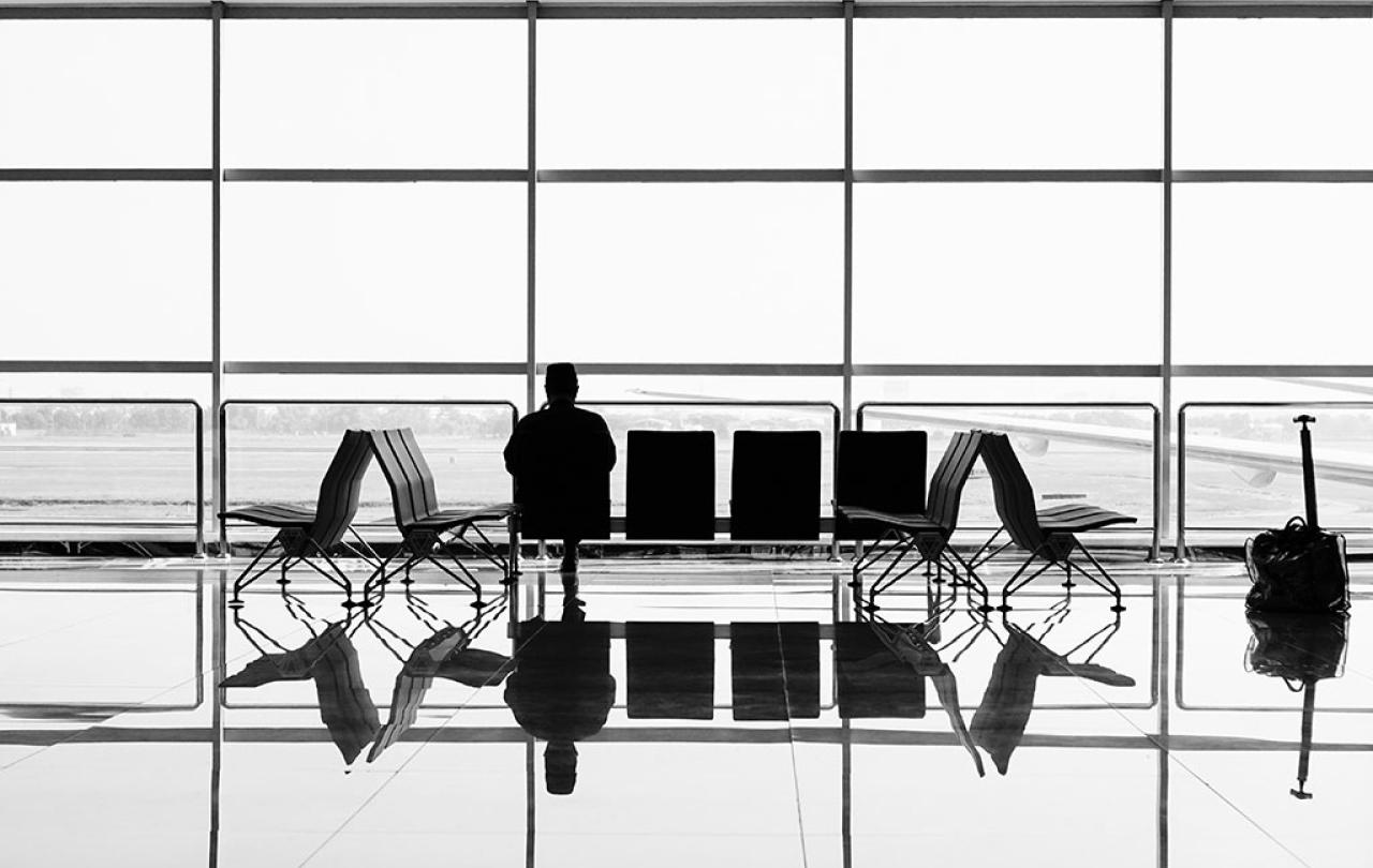 A large airport window silhouettes a bench at which one person sits.