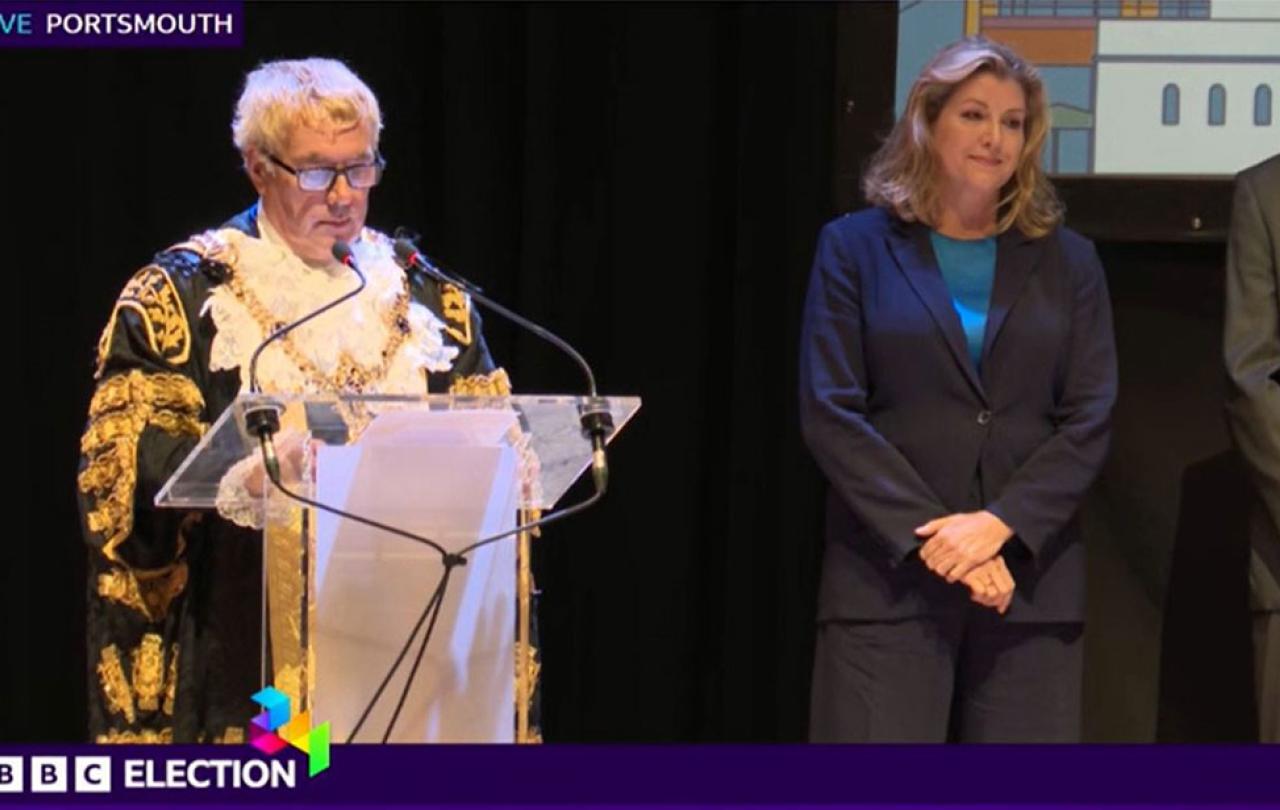 A mayor reads an election result as a despondent candidate looks on.