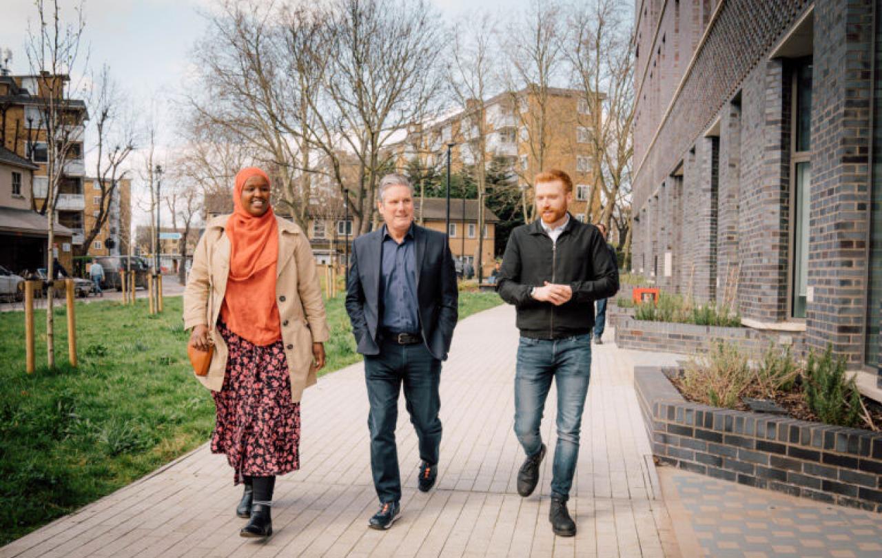 Kier Starmer walks along a residential development's path with two other people.