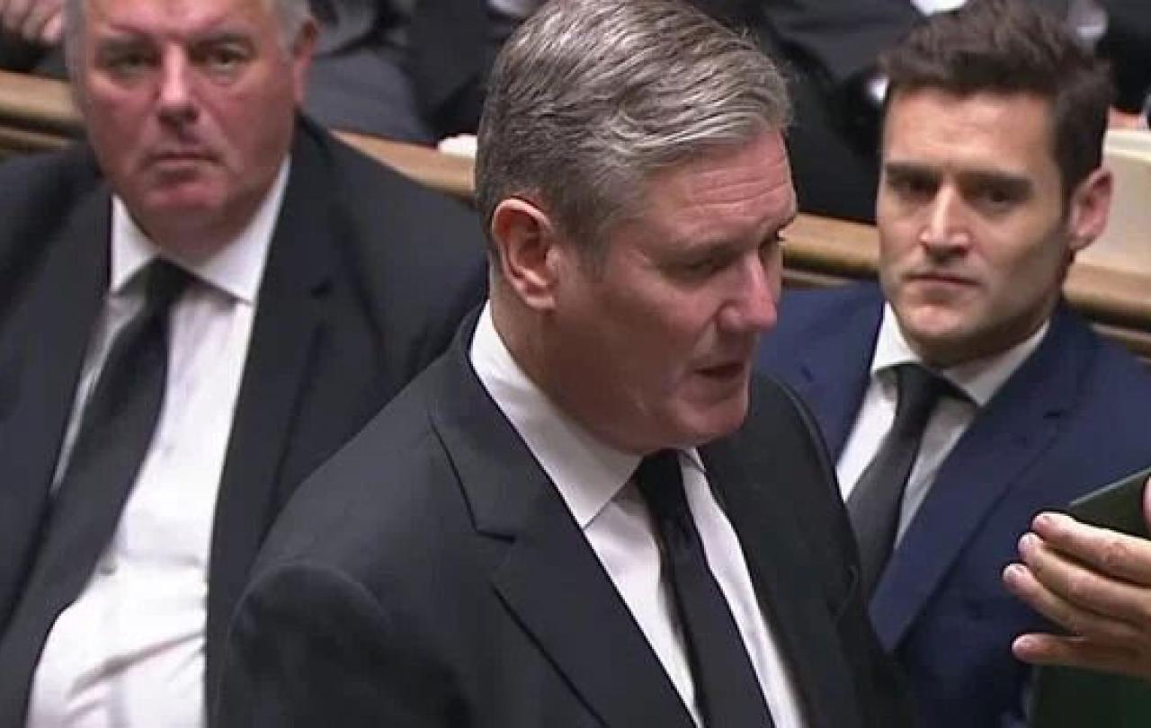 Keir Starmer stands in the House of Commons and recites an oath from a card held up in front of him.