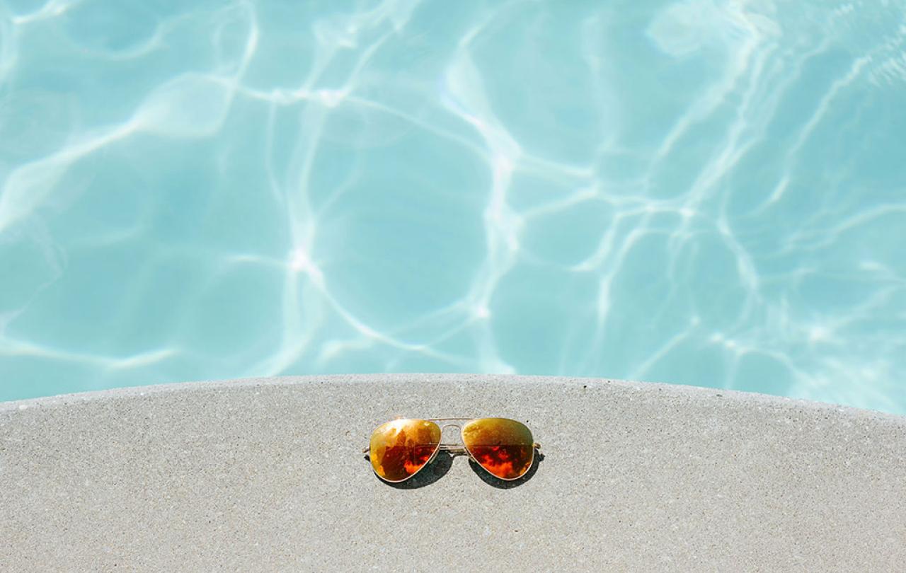 A pair of sunglasses beside a swimming pool.