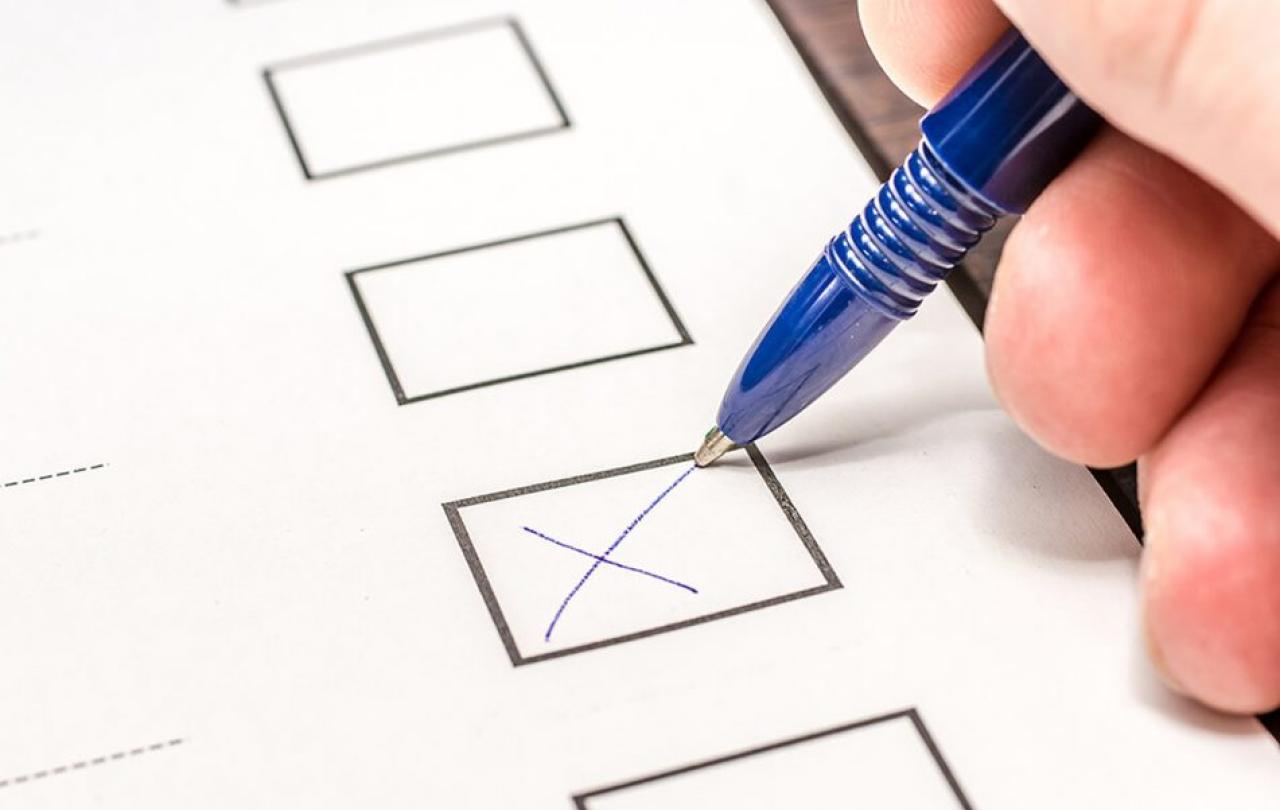 A pen draws a cross in a box on a ballot form.