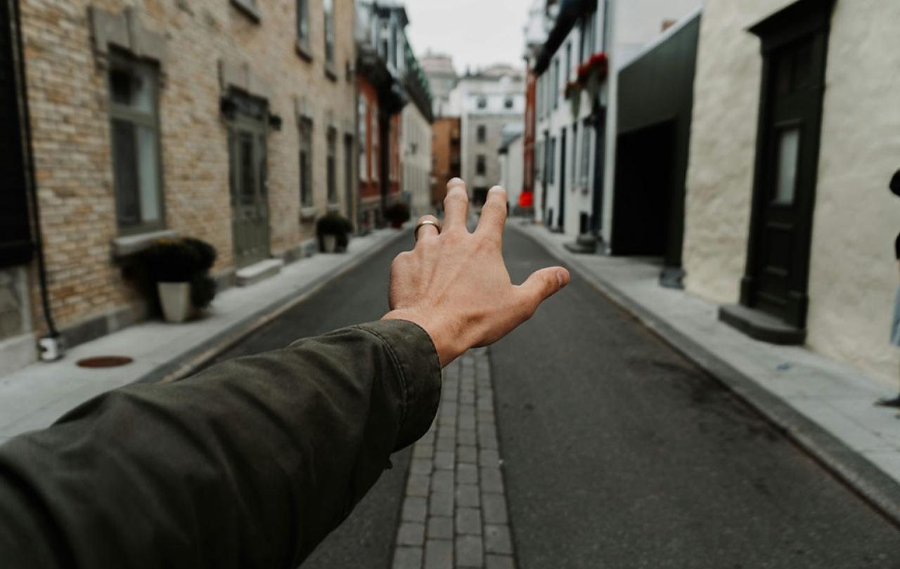 An arm and hand stretch out in front of some, a narrow street is the background.