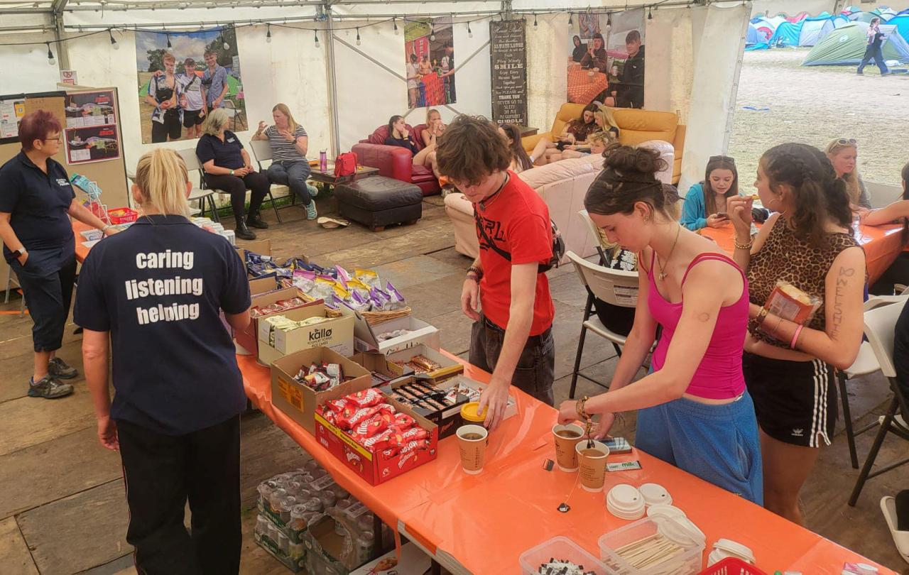 Festival goers, in a cafe tent, make drinks or sit around talking