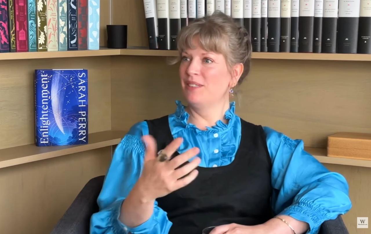 A woman being interviewed gestures with a hand in front of her