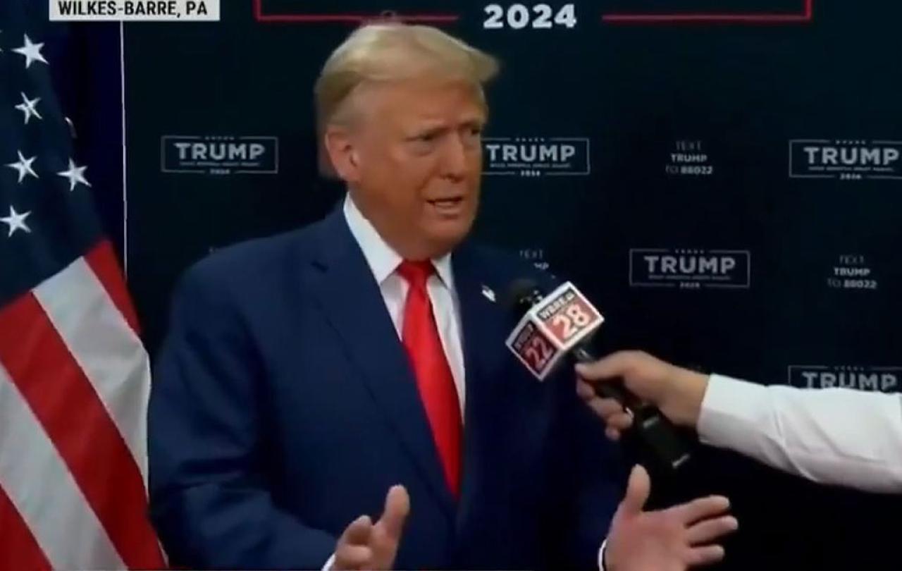 Donald Trump gestures with his hands while someone holds a mic in front of him,