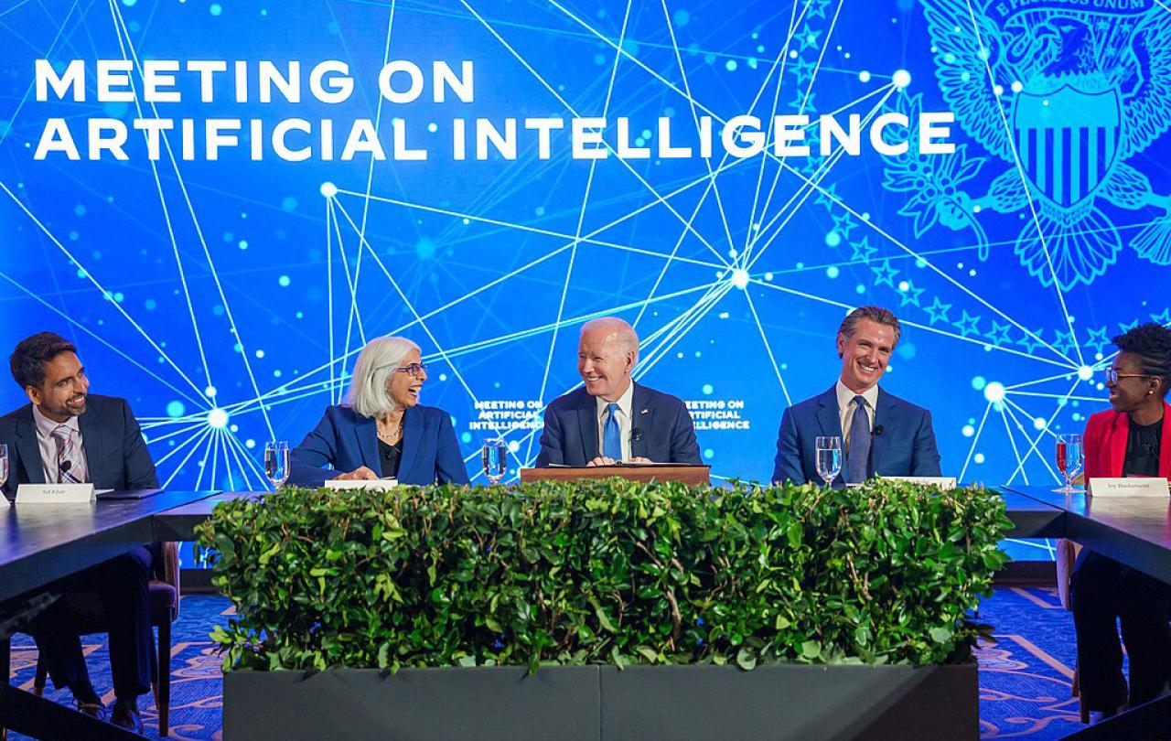 A board of experts sit at a table against a conference backdrop.