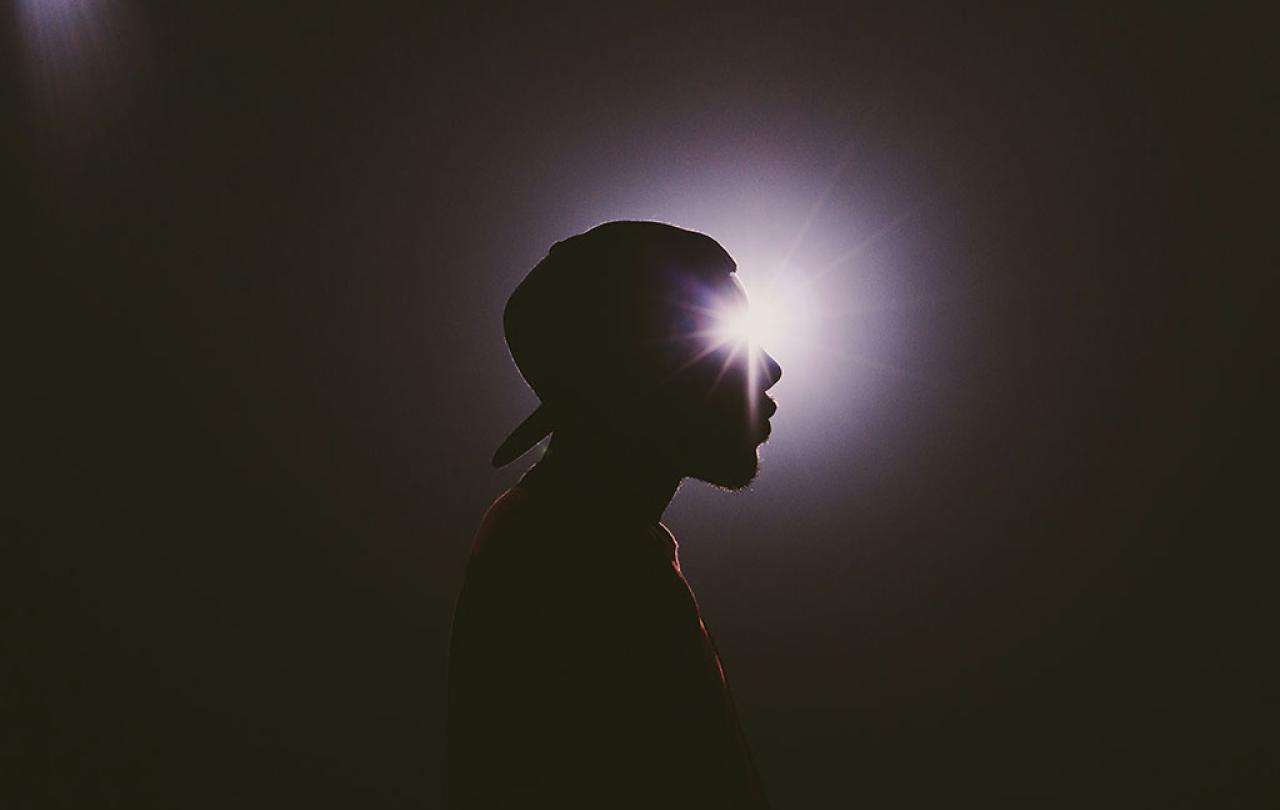 A star burst of light appears to emanate from the eye of a man's head in silhouette. 