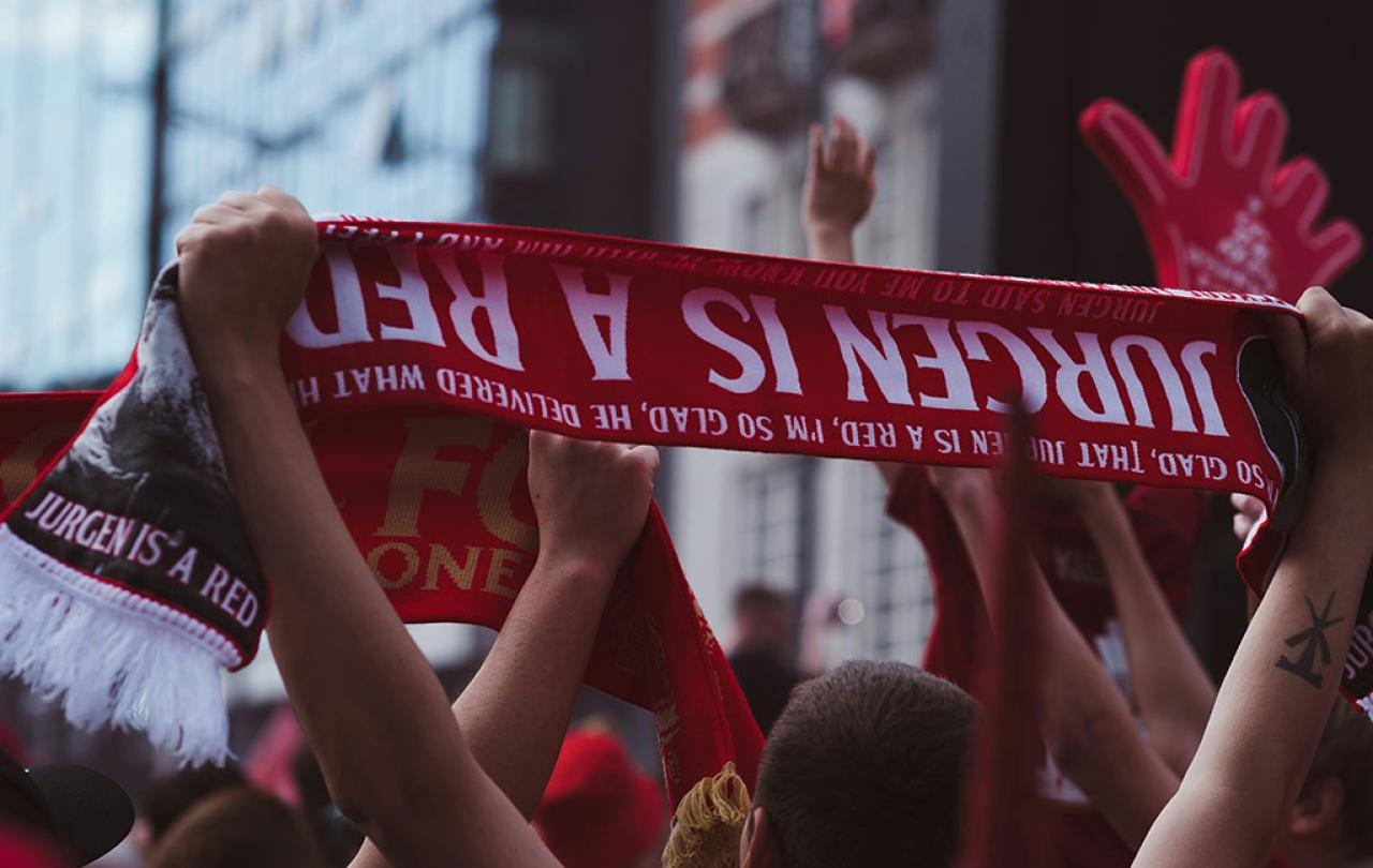 A fan holds an upside down football scrarf that reads 'Juergen is a red'.