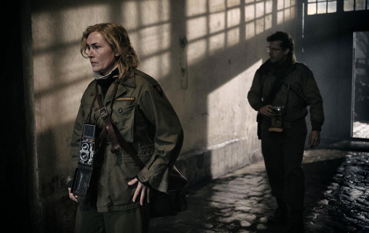 Two war photographers creep along a shadowy corridor.